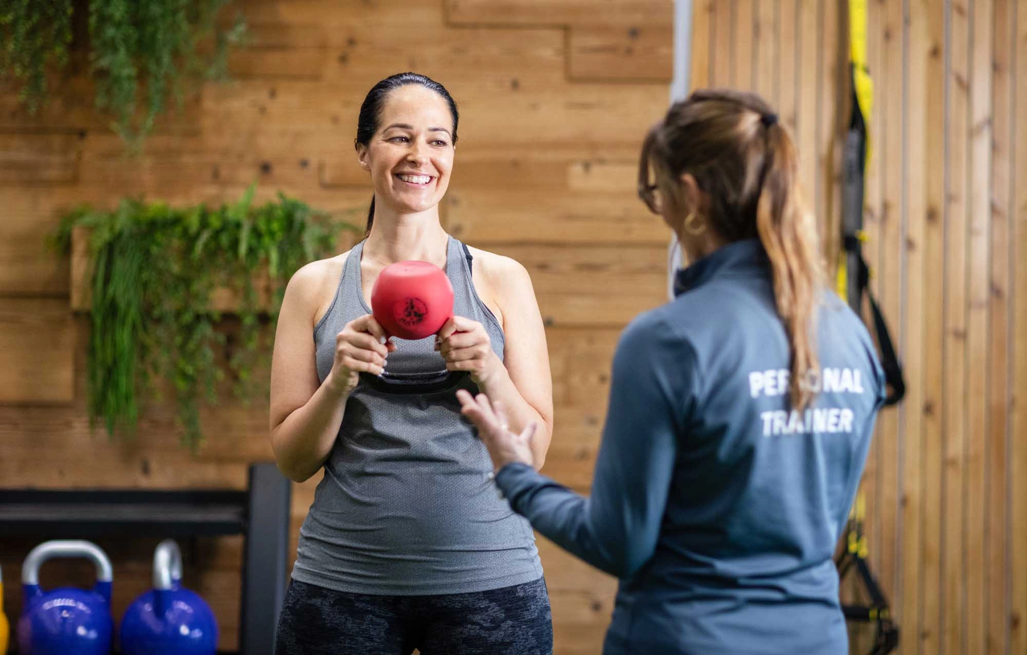 lady holding kettlebell with female personal trainer guiding her